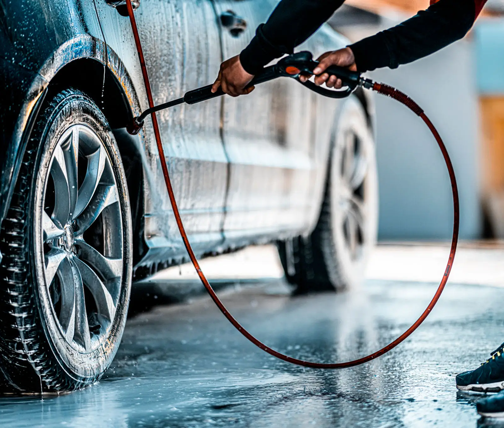 Person washing a car with a high-pressure hose.